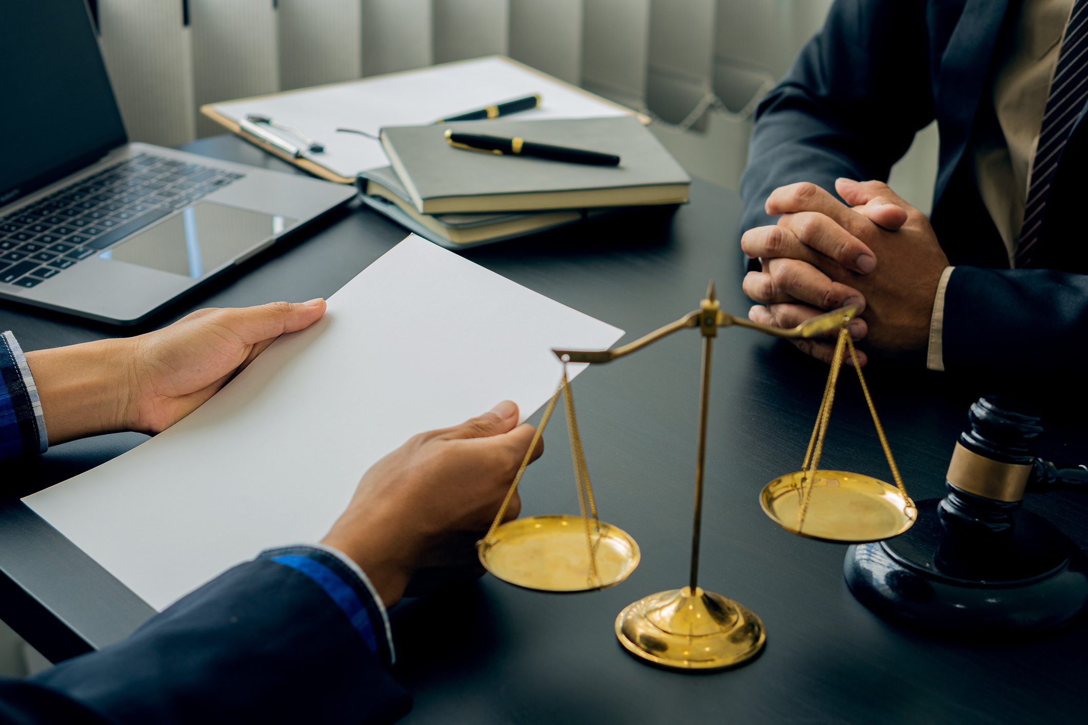 Lawyers discuss business contract documents sitting at a desk in the office of conceptual legal advice. Counselor with hammers and scales of justice on the table.